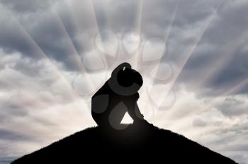 Silhouette of sad little girl sitting on a hill. Conceptual image