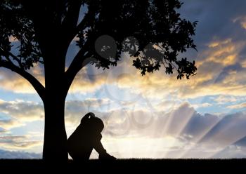 Silhouette of sad little girl sitting under a tree crying. Conceptual image of child abuse