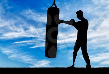 Silhouette of a disabled man with a leg prosthesis, training with a punching bag. The concept of disabled people who engage in sports