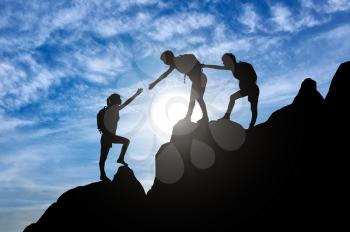 Silhouette of two female mountaineers helping another female mountaineer to overcome the obstacle in the mountains. Conceptual scene of a girl climbers