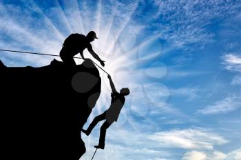 Silhouette of a climber who helps to climb the top of a man, throws him a rope and holds out his hand. Conceptual help scene