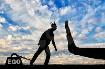 Silhouette of a selfish man with a crown on his head draws a heavy load - the ego and a large hand stop it. The conceptual scene of selfishness as a social problem