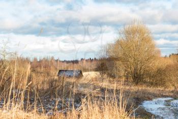 Beautiful winter landscape with a field, a house, a forest and a little snow on a sunny day.