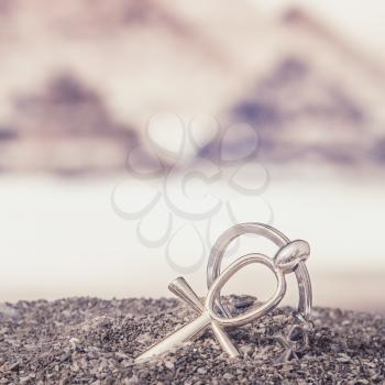 The Egyptian ankh is a cross in the sand against the backdrop of the Great Pyramids. Photo toned.