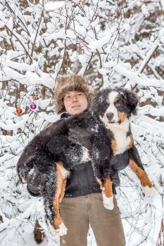 A man holds a dog breed mountain dog in winter forest.