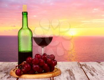 Bottle of wine with wine glasses at sunset on the sea background