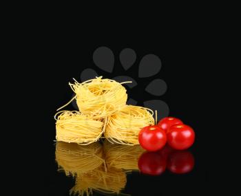raw dry nest pasta with reflection on black with tomato