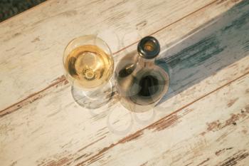 glass with white wine in vineyard on old table. Vineyard at sunset. White wine glass, wine bottle and white grape on wood table with copy space