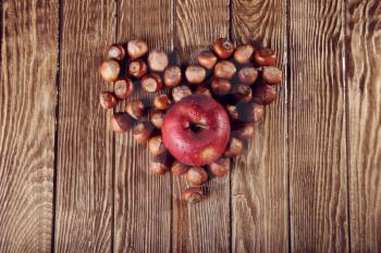 Autumn Collection. nuts and apple forming heart shape on wooden background