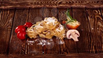 Top view on Raw homemade pasta with tomatoes, mushrooms, onions and flour over old wooden table