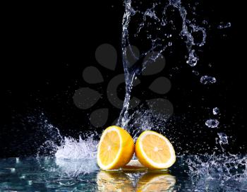 Sliced lemon in the water on black background. Fresh lemons with water splash. Dynamics of a liquid, juicy appetizing lemon and glass with splashed out water on a dark surface of a table