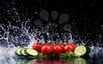 Studio shot with freeze motion of cherry tomatoes and slices of cucumber in water splash on black background