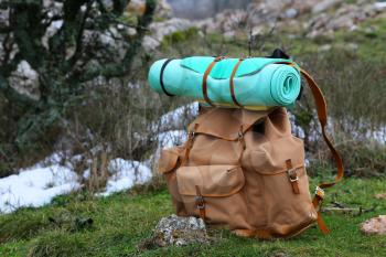 Tourist backpack and sleeping pad on a background of mountains. Outdoor wanderlust items. Travel, tourism and camping equipment. Picnic rest on the nature. Summer active hiking and trekking tools.