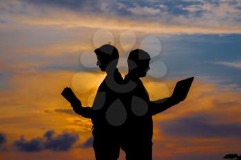 silhouette of a men with laptop and a book on sunset or sunrise background. The idea of the contradictions of the old and new values. The concept of old and modern