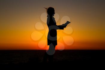 Teen girl reading book outdoors at sunset time. silhouette of a girl reading at sunset