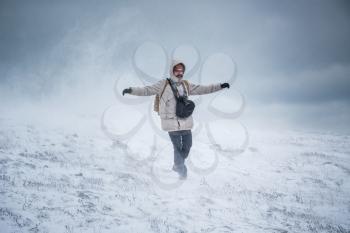 Wintery scene of shivering man in snowstorm or ice storm. Man walking in the snowstorm in the mountains