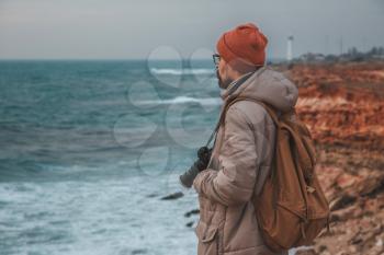 Man looking to lighthouse in seaside. Hipsters pictures of sea, sunset stony beach with the lighthouse in the distance