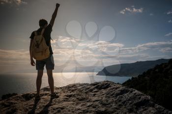 Hiker with backpack standing on top of a mountain with raised hands and enjoying view