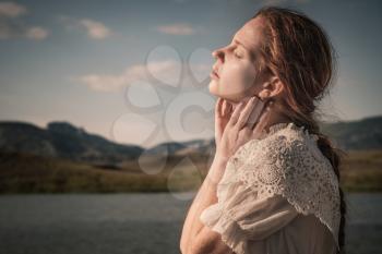 Beautiful young blond woman outdoors portrait near the lake. Red-haired girl with freckles in a white dress. The idea and concept of freedom and loneliness.