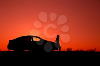 Young girl with and broken car. Silhouette of sedan car with girl on the background of beautiful sunset