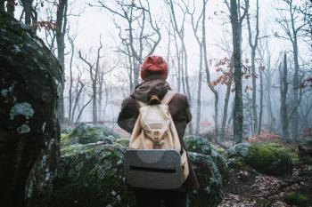 man walking on a dark path through a spooky forest. Hipster with a backpack behind his back goes on a trip