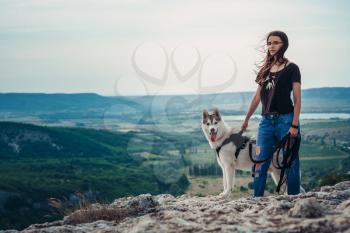 Beautiful girl plays with a dog (grey and white husky) in the mountains at sunset