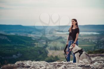 Beautiful girl plays with a dog (grey and white husky) in the mountains at sunset