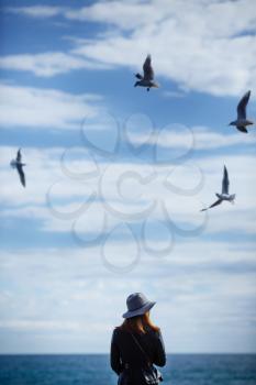 Girl looking at the calm sea on the with wind in her hair and seagulls on the background. Autumn in the Hat