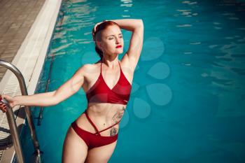 Enjoying suntan and vacation. Colorful portrait of pretty young woman in red swimsuit lying near swimming pool.