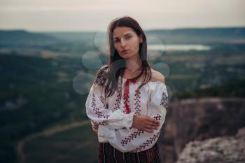 Atractive woman in traditional romanian costume on mountain green blurred background. Outdoor photo. Traditions and cultural diversity