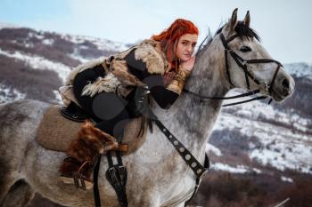 Beautiful girl on horse and with red hair in armor. Woman is a Viking. Fantasy