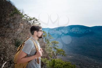 young hipster man in the spring mountains. Hipster with a backpack behind his back goes on a trip