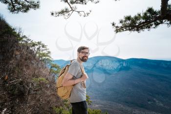 young hipster man in the spring mountains. Hipster with a backpack behind his back goes on a trip