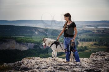 Beautiful girl plays with a dog, grey and white husky, in the mountains at sunset. Indian girl and her wolf