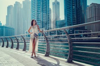 Happy beautiful unrecognizable tourist woman in fashionable summer white dress enjoying in Dubai marina in United Arab Emirates. Luxury and comfortable tourism season in UAE.