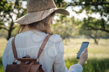 woman traveler with backpack and hat walking in amazing forest, wanderlust travel concept, atmospheric moment. earth day. use smartphone to find the way, map