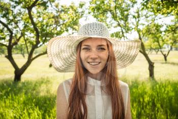 Girl in the hat and dress of the garden trees. red-haired young woman with freckles on vacation