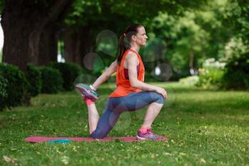 Young beautiful woman meditates on a summer day in the park. Idea and concept of calm in a busy city and a healthy lifestyle, stretching and preparing for a run in the park