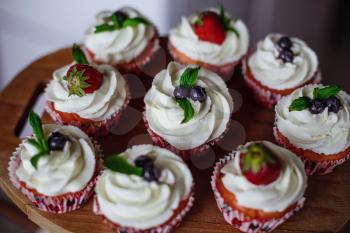 Tasty muffins decorated with red and blue berries and mint leaf. Homemade vanilla muffins with strawberry and blackberry
