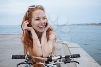 Beautiful woman riding on bike. Lifestyle and health in the city. Cheerful red-haired young woman gets pleasure from walking around the city