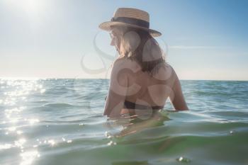 Beautiful woman having a fun while swimming in the sea. Beautiful romantic lady in a hat resting at sunset