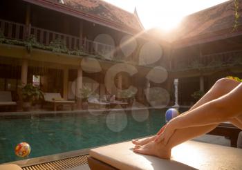 Beautiful tanned women legs by the swimming pool. soft beautiful light at sunset in a hotel in traditional Thai style, rest in an exotic