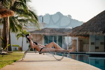 Shot of a young woman relaxing by the luxury pool. Summer vacation. Happy woman enjoying sunny summer day at the poolside