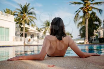 Shot of a young woman relaxing by the luxury pool. Summer vacation. Happy woman enjoying sunny summer day at the poolside