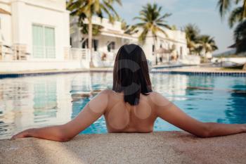 Shot of a young woman relaxing by the luxury pool. Summer vacation. Enjoying vacation. Back view of slim young woman drinking cocktail in swimming pool.