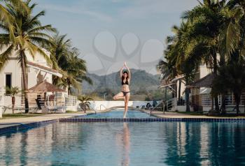 young woman practicing pose yoga on swimming pool and the nature beach at sunset or sunrise. Yoga and Healthy Concept. yoga in tree pose