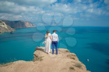 Beautiful smiling young bride and groom walking on the beach, kissing and having fun, wedding ceremony near the rocks and sea. Wedding ceremony on coast of Cyprus