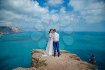 Beautiful smiling young bride and groom walking on the beach, kissing and having fun, wedding ceremony near the rocks and sea. Wedding ceremony on coast of Cyprus