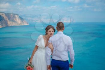 Beautiful smiling young bride and groom walking on the beach, kissing and having fun, wedding ceremony near the rocks and sea. Wedding ceremony on coast of Cyprus