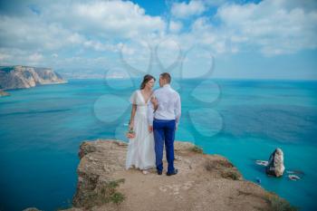 Beautiful smiling young bride and groom walking on the beach, kissing and having fun, wedding ceremony near the rocks and sea. Wedding ceremony on coast of Cyprus